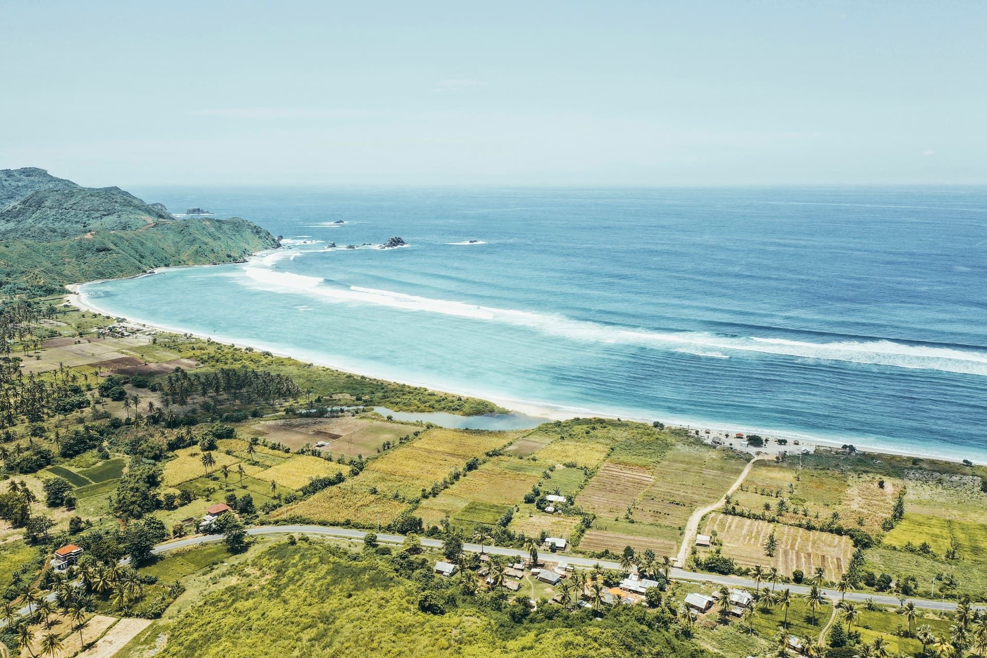 Aerial view of the Lombok coastline, green farmland meeting a long surf beach